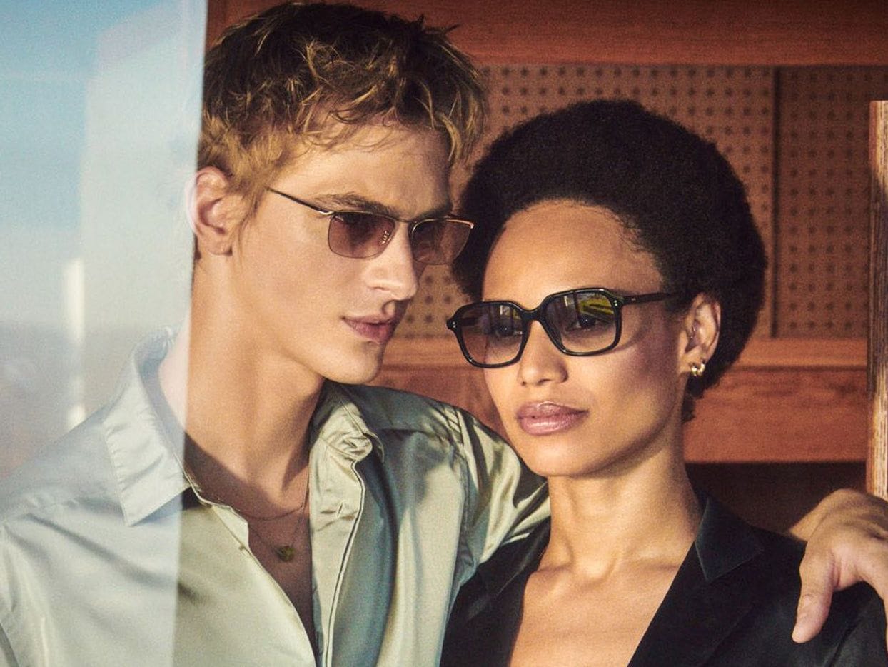 A man and a woman wearing Oliver Peoples glasses and sunglasses