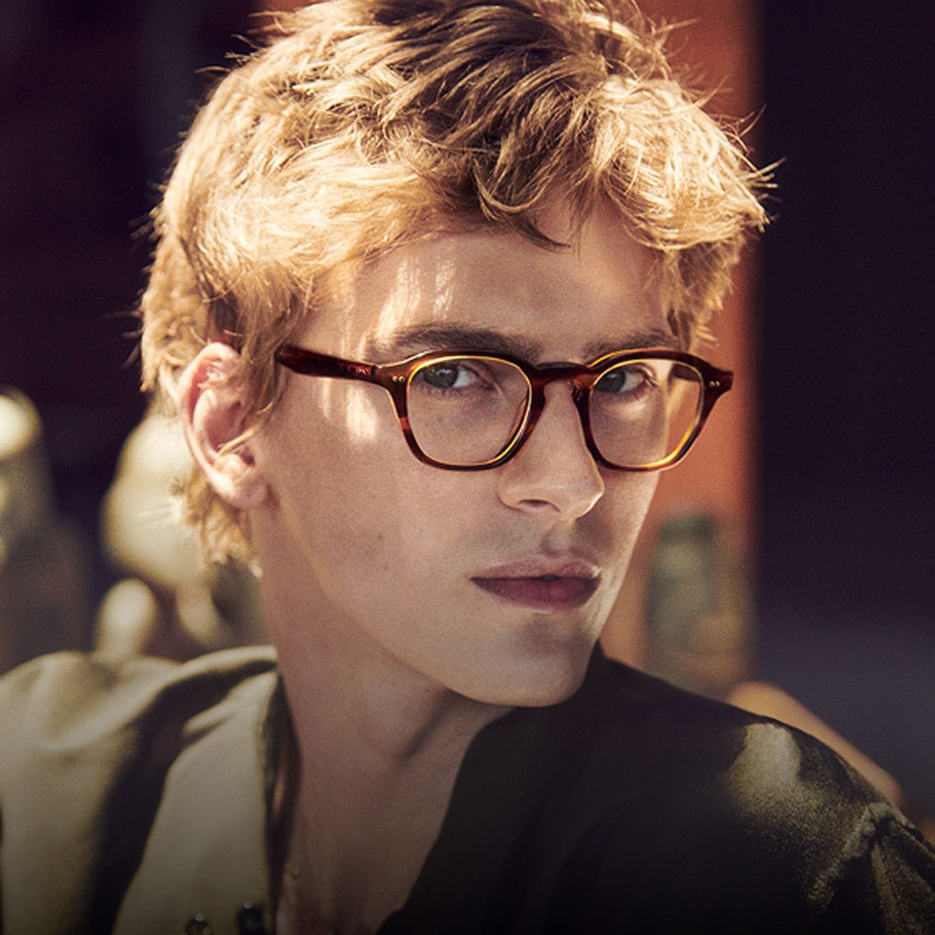 A young man in tortoiseshell Oliver Peoples glasses, lit by warm sunlight