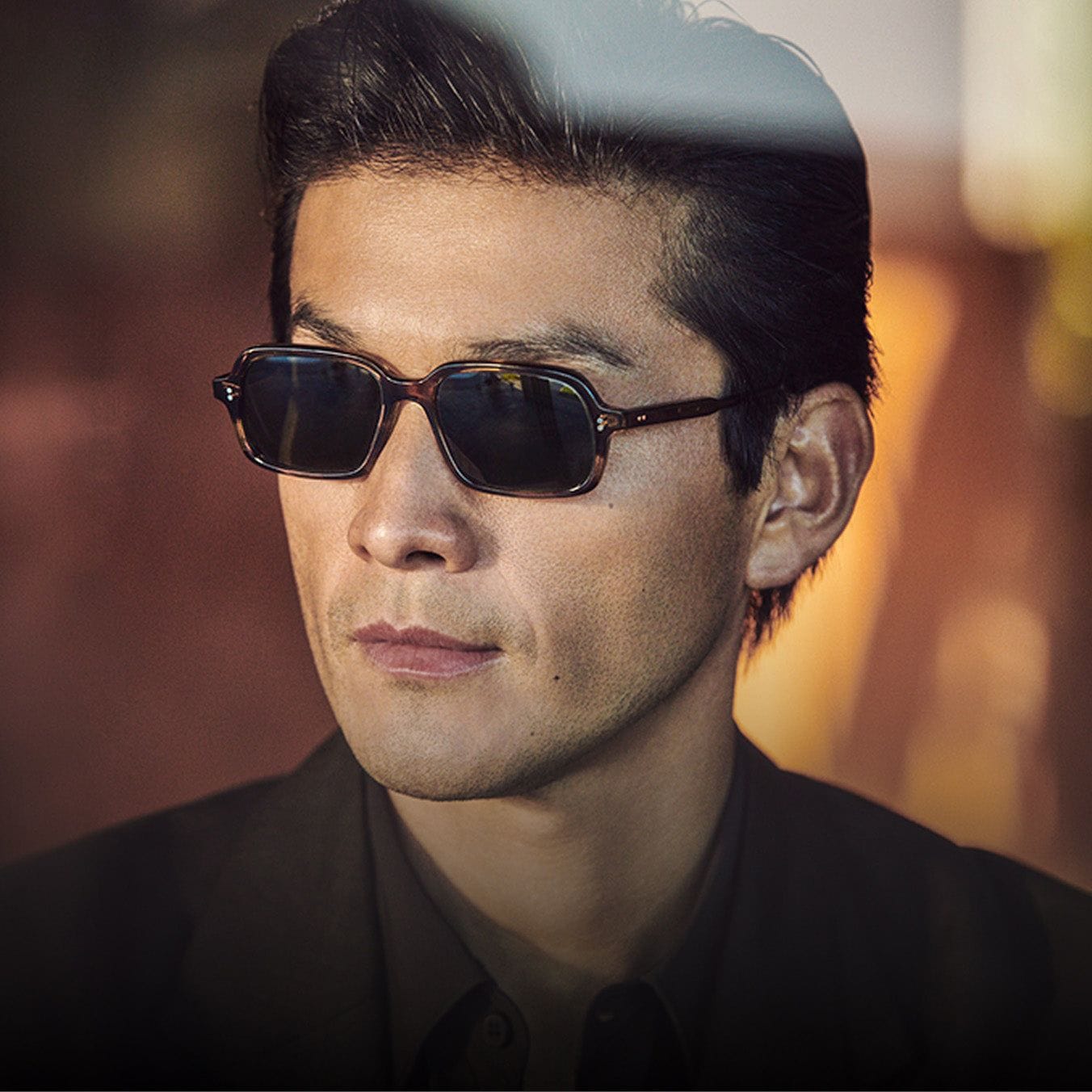 A man in dark Oliver Peoples sunglasses in golden light