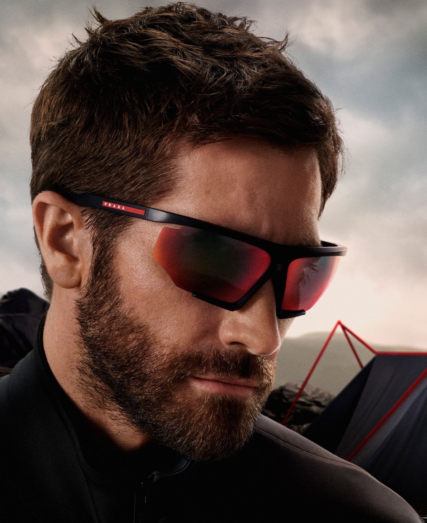 A bearded man wearing Prada Linea Rossa sunglasses with red-tinted lenses