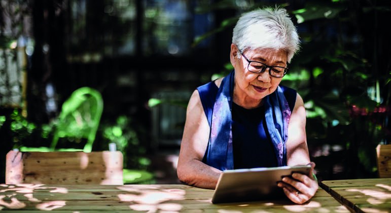 A woman in glasses reading a tablet at a garden table
