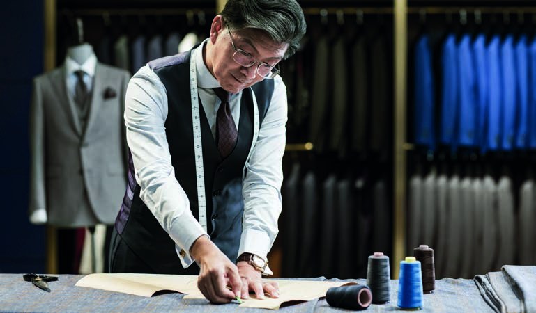 A tailor in glasses measuring cloth at a cutting table